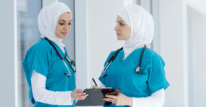 Two Saudi Arabian doctors talk to each other while looking over a clipboard of paperwork