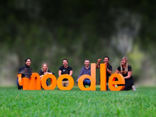 Menschen, die hinter einem Bild mit riesigen „Moodle“-Buchstaben stehen