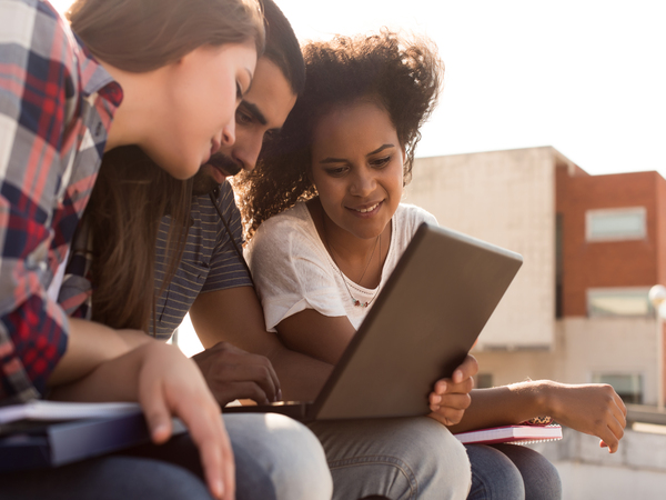 Drei Studenten teilen sich einen Laptop-Bildschirm auf dem Campus