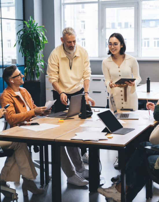 Miembros del equipo reunidos en una mesa de reuniones con ordenadores portátiles y documentos mientras intercambian ideas sobre un nuevo proyecto.