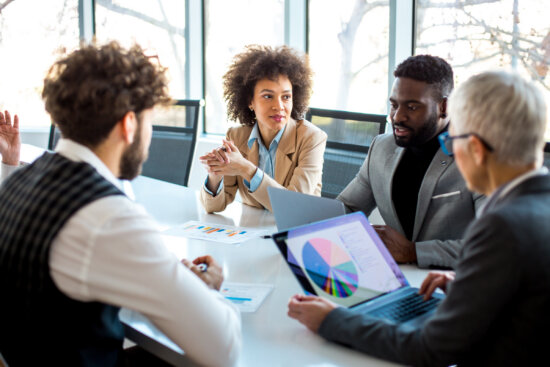 Une femme et trois hommes sont assis autour d'une table de réunion. L'un des hommes a ouvert son ordinateur portable, sur lequel s'affiche un diagramme circulaire. Image